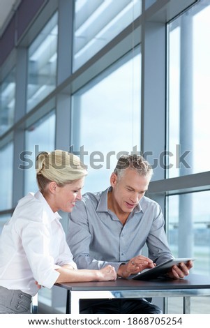 A vertical view of a businessman and businesswoman using a digital tablet while sitting at the table near a glass window