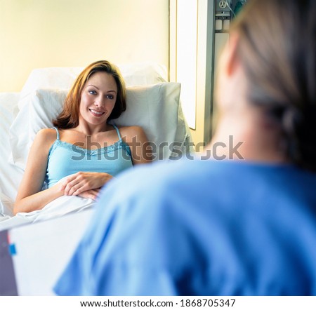 A patient lying on a bed while smiling at a doctor making rounds in the hospital doorway