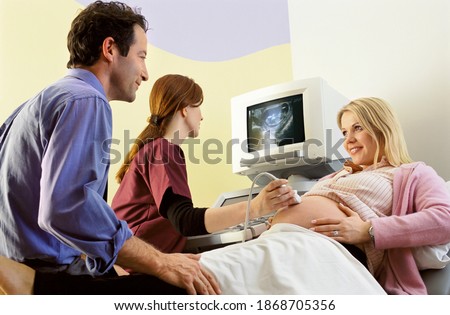 A qualified nurse performing an ultrasound examination on a pregnant woman with her smiling husband sitting next to her