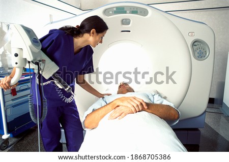 A qualified technician in scrub suit guiding a patient into the MRI scanner at the hospital