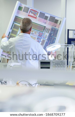 A vertical rear view of an Engineer examining the circuit diagram in a laboratory