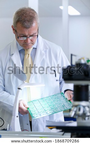 An Engineer with eyeglasses carefully examining a circuit board under the magnification lamp in a laboratory
