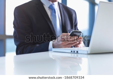 A closeup of a cell phone and a laptop at the table being used for text messaging by the Businessman