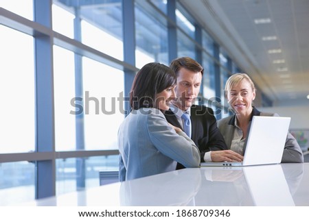 A group of business people in formal suits using a laptop at a desk counter in the office