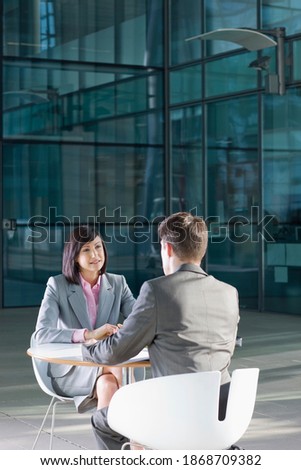 A vertical view of a Businesswoman and a businessman having a meeting at a table outside the building