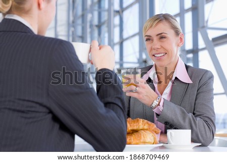 A smiling businesswoman enjoying the breakfast of coffee and croissants with her co-worker while holding a glass of juice in the cafeteria