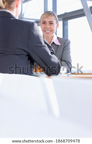 A smiling businesswoman enjoying her breakfast of coffee and croissants with her co-worker in a cafeteria