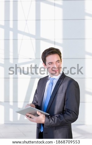 A vertical view of a confident businessman in formal suit using a digital tablet