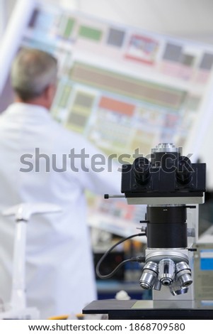 A vertical view of an engineer examining the circuit diagram in a laboratory with a microscope in the foreground