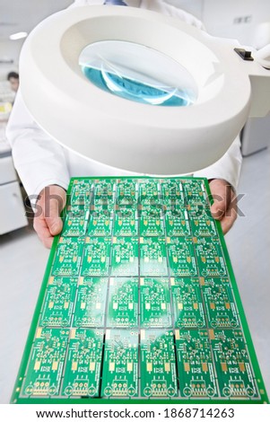 A circuit board being held and examined by an engineer under the magnifying lamp in a laboratory