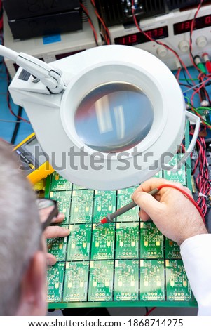 An Engineer examining the circuit board through a magnifying lamp on an electrical test bench