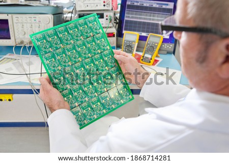 A high angle view of an engineer examining the printed circuit board at an electrical test bench equipped with oscilloscope and multimeters
