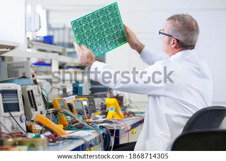 An expert engineer in a lab coat examining the printed circuit board at an electrical test bench