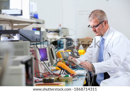 A side view of an engineer working at the electrical test bench with multimeters and test probes next to an oscilloscope