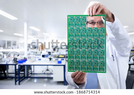 A portrait of an engineer holding a printed circuit board while looking through the gaps in a laboratory
