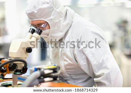 A horizontal view of a scientist in clean suit looking into a microscope to examine the silicon wafer in a laboratory