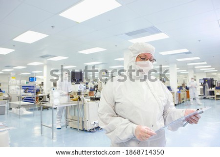 Scientist in clean suit looking down at a report attached to a clipboard in the silicon wafer manufacturing laboratory