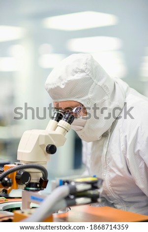 A vertical view of a scientist in clean suit looking into a microscope to examine the silicon wafer in a laboratory