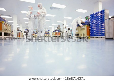 A low angle view of scientists in clean suits discussing a report in the silicon wafer manufacturing laboratory