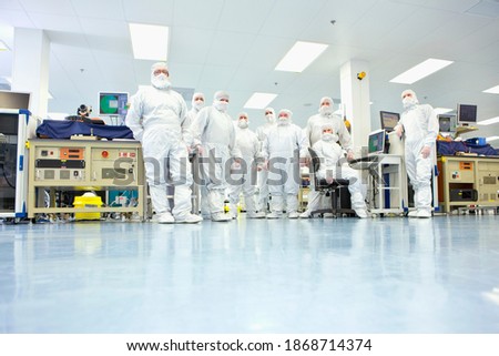 A low angle group portrait of engineers wearing clean suits in a silicon wafer manufacturing laboratory