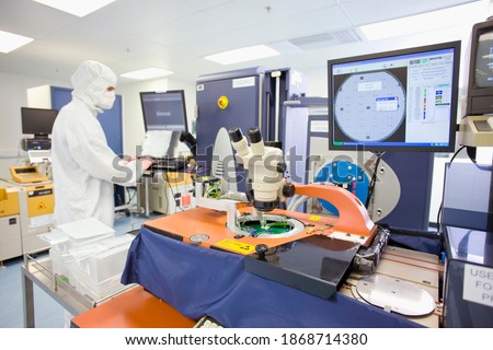 An engineer in clean suit working on a computer in a fully equipped silicon wafer manufacturing laboratory