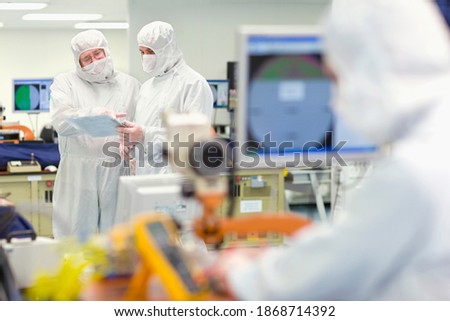 A horizontal view of scientists in clean suits discussing paperwork in a silicon wafer manufacturing laboratory with selective focus