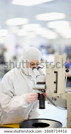 A scientist in a clean suit carefully examining the silicon wafer under a microscope while adjusting the lens in a laboratory