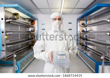 A front view portrait of a scientist in a clean suit holding a container in a silicon wafer manufacturing laboratory