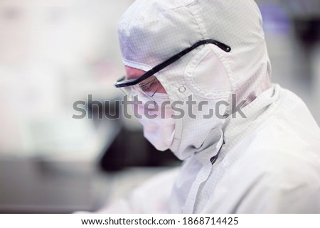 A side profile close-up of a scientist in a clean suit and protective eyeglasses working in the silicon wafer manufacturing laboratory