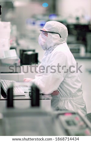 A vertical side-view of a scientist in a clean suit attentively working on the computer in a silicon wafer manufacturing room