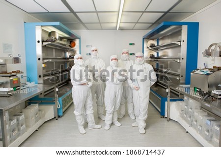 A portrait of scientists in clean suits standing together in a silicon wafer manufacturing laboratory
