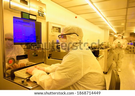A scientist in a clean suit working on a computer in the silicon wafer manufacturing room with warm light