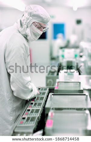 A scientist in lab suit and safety eyeglasses watching the silicon wafers being processed in a clean room laboratory