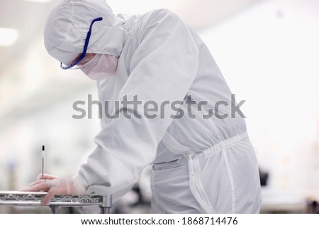 A horizontal side view of an engineer in a clean suit taking notes in the silicon wafer manufacturing laboratory