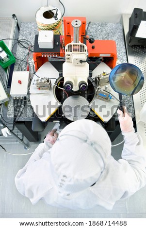 A vertical view from top with Reflection of the scientist on a silicon wafer next to the microscope in a special laboratory