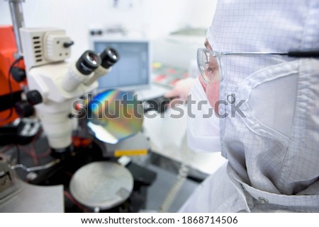 Close up of a scientist in clean suit with selective focus examining the silicon wafer under a microscope in a special laboratory