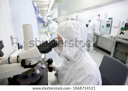 A horizontal view of a scientist in a clean suit examining the silicon wafer under a microscope in a special laboratory