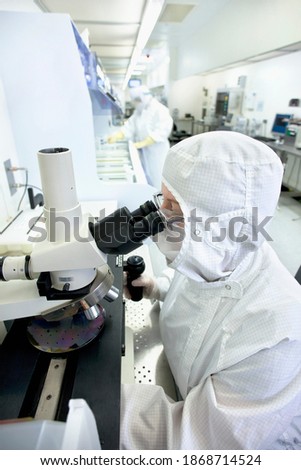 A high angle view of a scientist in a clean suit examining the silicon wafer under a microscope in a special laboratory