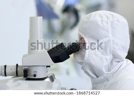 A side view close-up of a scientist in a clean suit examining the silicon wafer under a microscope in a special laboratory