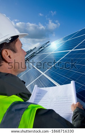 A vertical over the shoulder shot of an engineer holding a blueprint in front of a large solar panel