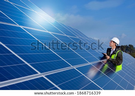 A side profile medium shot of an engineer using tablet while inspecting a large solar panel.