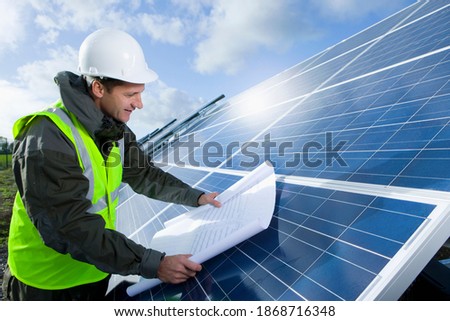A medium shot of a happy engineer looking at blueprint on a large solar panel.