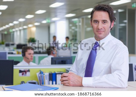 A portrait of confident businessman standing in formal wear at the counter in a telemarketing office
