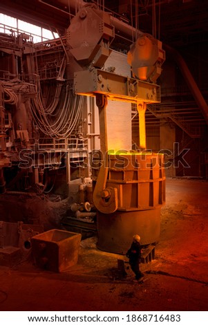 A wide vertical shot of an engineer looking at a big vessel holding forged steel in a foundry.