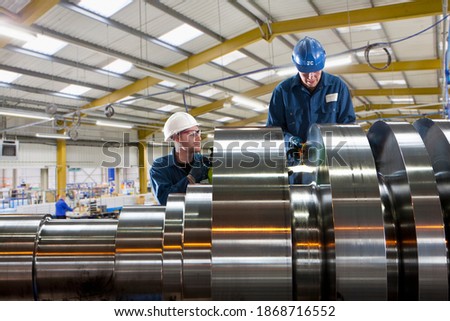 A medium shot of two engineers in coverall cleaning a big cylindrical machinery in a factory.