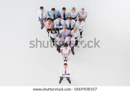 Horizontal overhead shot of a group of businesspeople standing in an inverted pyramid formation behind their boss who smiles at the camera.