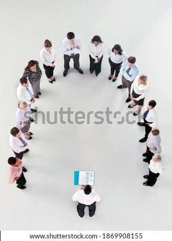 Overhead shot of a group of businesspeople standing in a horseshoe formation listening to a businessman reading a report.