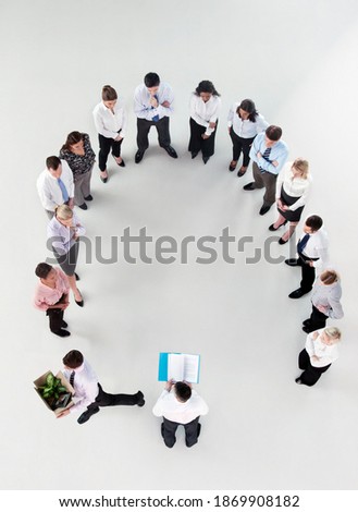 Overhead shot of a group of businesspeople standing in a horseshoe formation listening to a businessman reading a report as a colleague walks away with his belongings being fired.