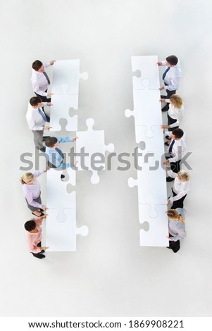 High angle shot of a group of businesspeople with large jigsaw pieces in two rows standing face to face with a businessman moving his jigsaw piece to merge with the opposite side.