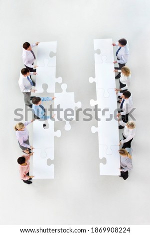 Overhead shot of a group of businesspeople with large jigsaw pieces in two rows standing face to face with a businessman moving forward.